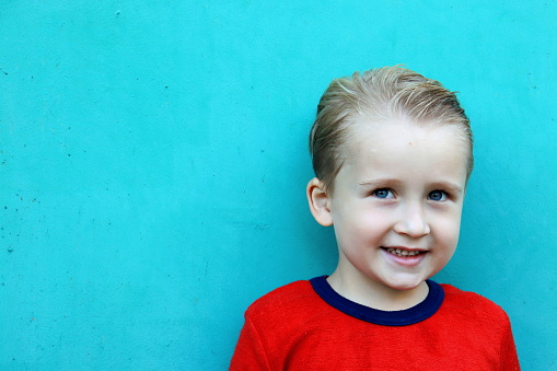 portrait of a cute boy with blond hair in a red T-shirt against a turquoise background