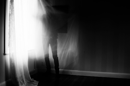 Artistic image with motion blur and grain of person standing in front of window, spooky feeling.