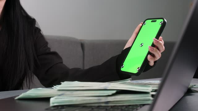 The woman taps the screen and with each tap money appears. View of a woman's hands on a phone with a green screen for copying. Loan, deposit, business and finance concept.