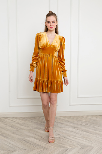 Blonde young woman wearing gold color dress. Long sleeve velvet dress. Orange high heels.