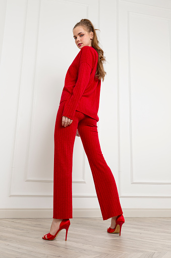 Blonde young woman wearing sweater and woolen trousers. Red wool fabric tracksuit.