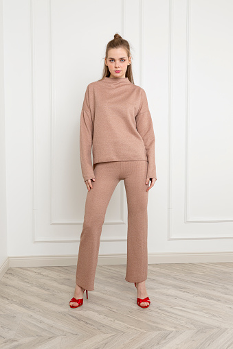 Blonde young woman wearing sweater and woolen trousers. Cream color wool fabric tracksuit.