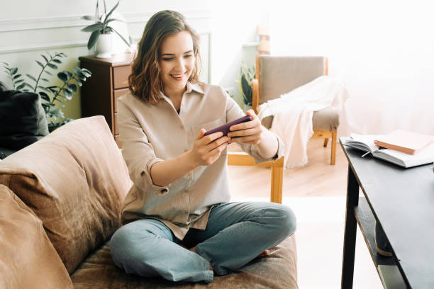 woman embracing digital connection. reading messages, socializing on social media, and playing mobile games on smartphone. happy young female engaging in modern digital communication and entertainment - young adult reading newspaper the media imagens e fotografias de stock