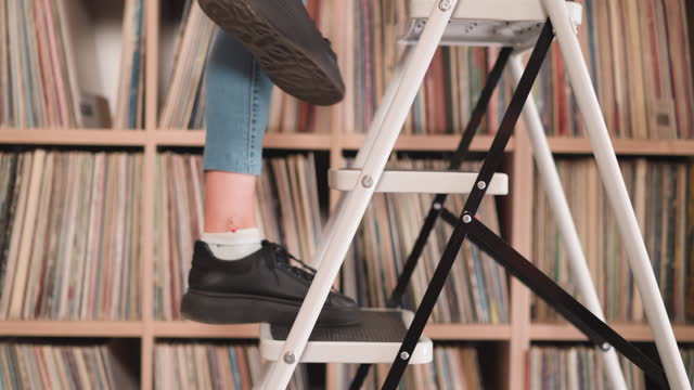 Woman goes up step ladder near bookcase