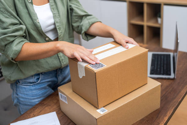 istock Woman hand apply QR code sticker to parcel, showcasing online shopping and e-commerce delivery. 1932232163