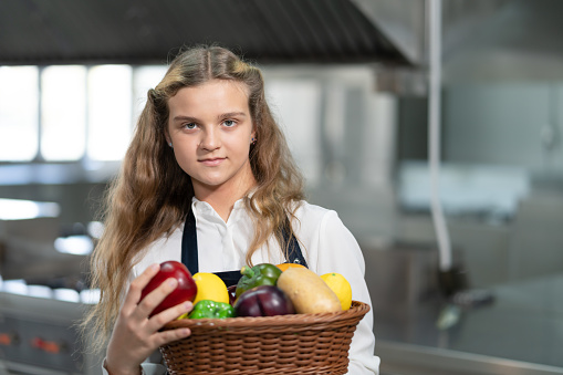 Portrait of student girl chef holding basket fresh organic vegetables in kitchen