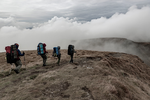 Group of hikers on the mountain range with strong wind and low clouds. Rainy weather, mute colors