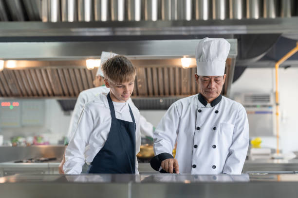 istock Student boy studying cooking in class at school kitchen. Senior Asian teacher chef teaching cooking to children. Education Concept 1932265668