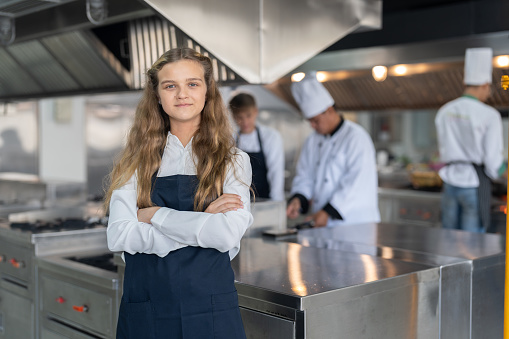 Portrait of student girl chef wearing apron standing with crossed arms study cooking class in kitchen at school