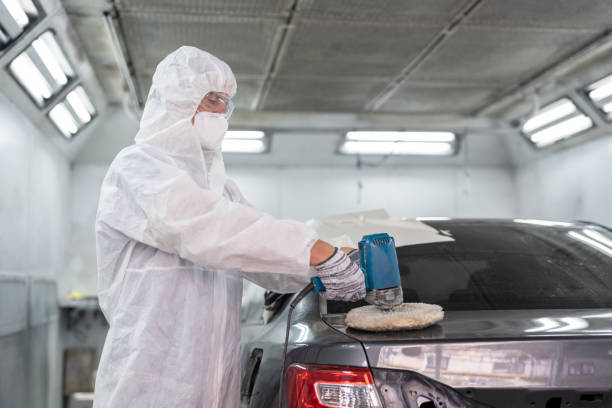istock Painter man in protective workwear using a polishing machine polish car body after painting finished in the chamber at auto car garage service. 1932275330