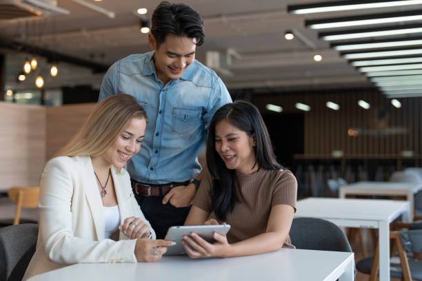 istock Diverse group of young women and man enjoying and looking in tablet computer on table at modern workplace. Businesspeople working on social media strategy using a digital tablet. 1932276940