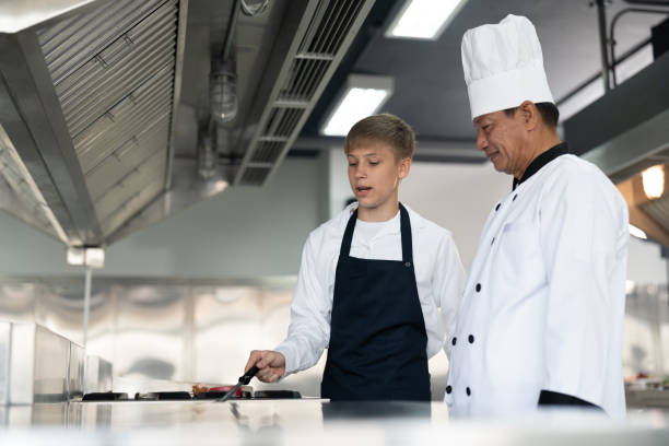 student boy studying cooking in class at school kitchen. senior asian teacher chef teaching cooking to children. education concept - chef trainee cooking teenager imagens e fotografias de stock