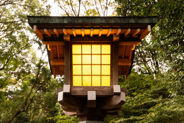 A Traditional Japanese Wooden Lantern glowing in the evening with green trees behind.