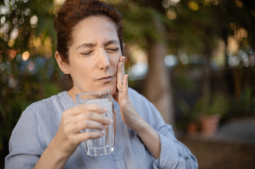 Caucasian woman reacting with tooth pain after taking a sip of ice cold water, part of a series for sensitive teeth