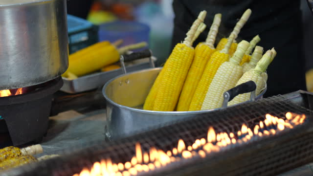 A close-up shot of a stall vendor boiling sweet corn in hot pot, preparing food and ready for sale at an Asian night market.