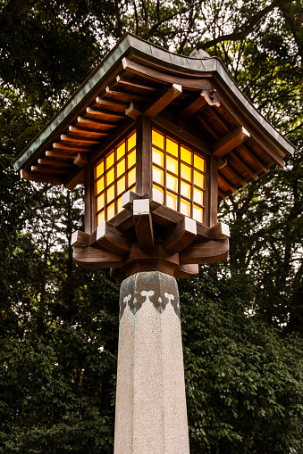 A Traditional Japanese Wooden Lantern glowing in the evening with green trees behind.