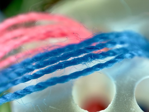 A closeup shot of red, purple, and blue knitting yarns and crochet hooks on a white surface