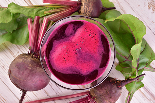 Beetroots on wooden background with spinach leaves, carrot, one rose, and a full glass of smoothie Rustic style. Top view. Copy space.