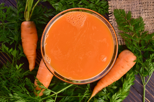 A glass of carrot juice on a dark wooden background. Flat lay.