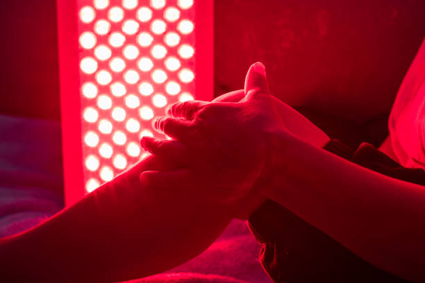 closeup of sore leg of a person treating with the red light therapy panel - alternatieve-therapie-fotos stockfoto's en -beelden