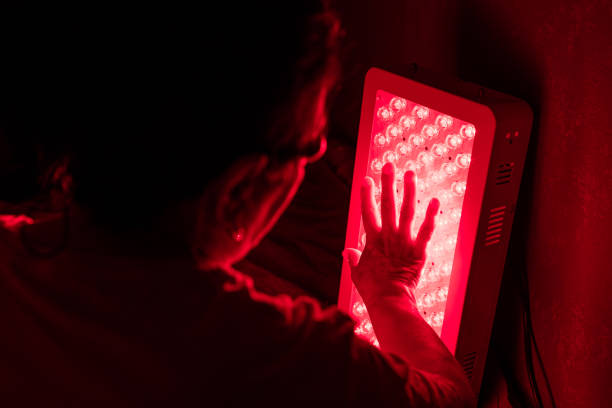 istock Closeup of Senior Woman touching Red Light Therapy Panel LEDs with hand 1932414630