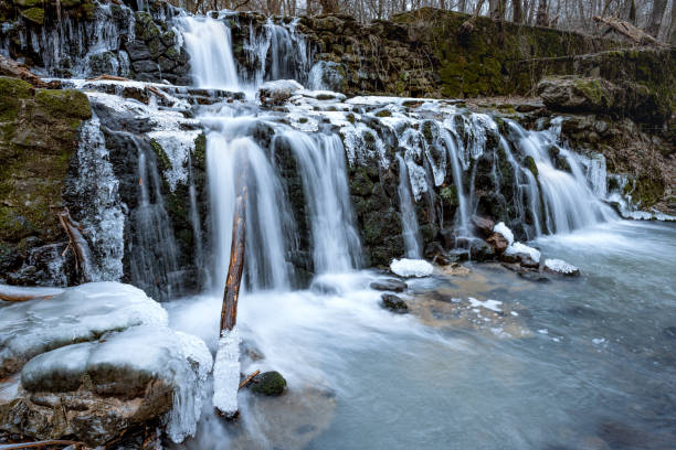 Icicles hang from the side of a waterfall, creating a stunning winter scene. The waterfall is located in a mountainous area, and the rocks are covered in ice. Hungary