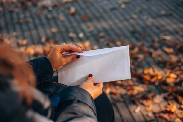 istock Woman opens a white envelope with a letter. Autumn foliage in the background. 1932460232