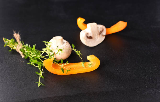 Mushrooms champignons and paprika with thyme sprig on a dark background.