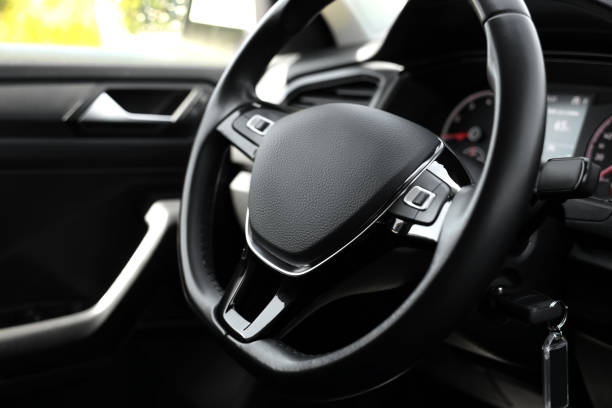 Part of the car steering wheel, covered with leather, with decorative seams, against the background of the car interior with console elements.