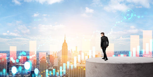 Side view of young businessman looking at financial charts in city sky. Concept of global stock market and trading