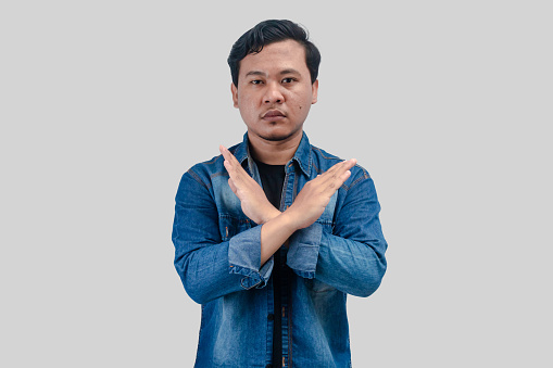Young Asian Man unhappy or confident standing wear holding two cross arms say no X sign, On isolated background