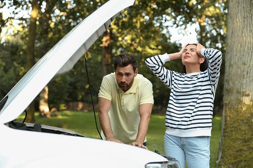 Stressed couple near broken car outdoors on summer day