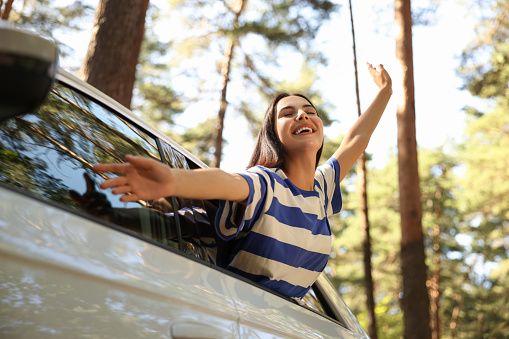Enjoying trip. Happy young woman leaning out of car window, low angle view