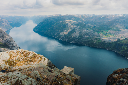 Drone panoramic photo of tourist in distant on the cliff contemplating a view of scenic fjord with crystal blue sea and Mountain View from above during summer time in South Norway, Scandinavia