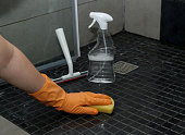Close up of woman's hand in orange gloves cleaning dirty shower floor tiles with lime remover