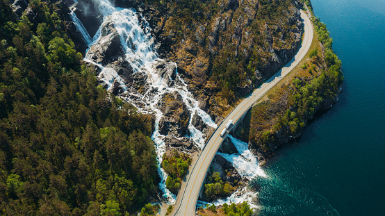 Drone high-angle photo of large motor vehicle on the curve road above the beautiful Langfoss waterfall with view of beautiful fjord  in South Norway