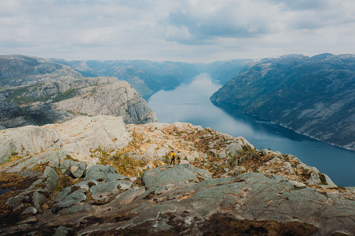 Done high-angle photo of heterosexual couple of backpackers getting to the edge of the cliff admiring beautiful landscape of mountain fjord during sunrise in South Norway, Scandinavia