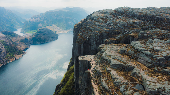 Drone panoramic photo of crowds of tourists on the cliff with view of scenic fjord with crystal blue sea and Mountain View from above during summer time in South Norway, Scandinavia