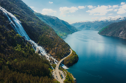 Drone high-angle photo of motor vehicle on the curve road above the beautiful Langfoss waterfall with view of beautiful fjord  in South Norway