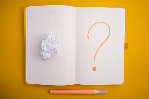 Notepad with a question mark on a yellow background. View from above. Ideas concept
