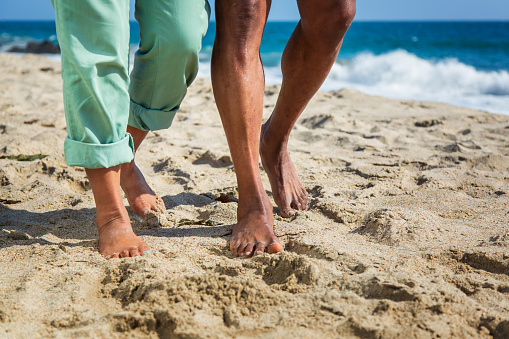 Legs of senior African American couple walking with at sandy beach. Model released.