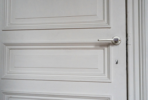 A white wooden door with a black metal handle. Door handle and interior fittings close-up.