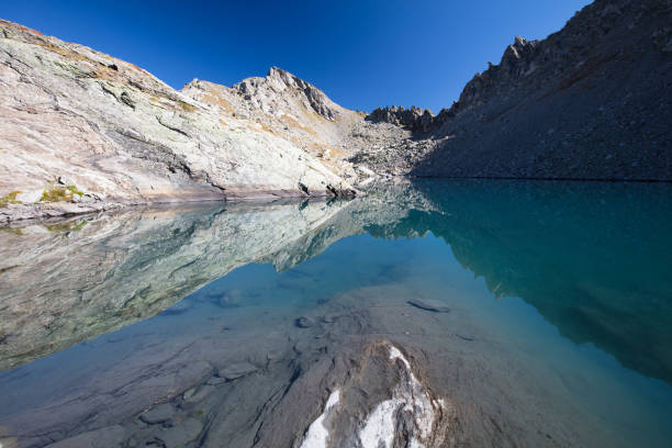 The surrounding mountain peaks are reflected in the calm blue waters of the mountain lake called Lago di Pietra Rossa, in a sunny day of early autumn.