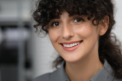 Portrait of confident businesswoman on blurred background. Beautiful lady with curly hair smiling and looking into camera. Space for text