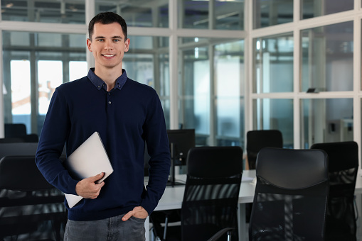 Happy man with laptop in office, space for text