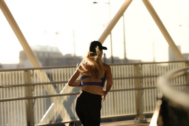 Rear view of a blond woman running on the ramp with white metal construction during summer afternoon.