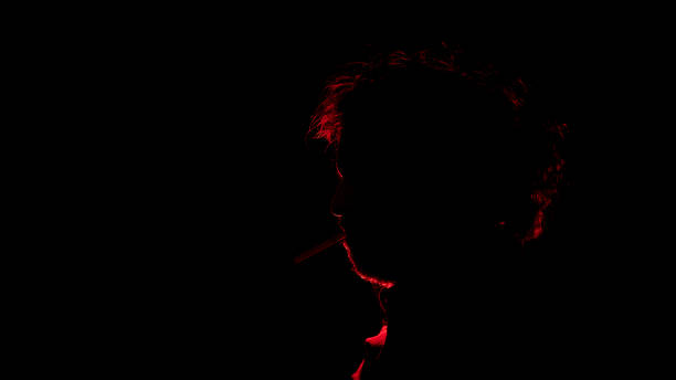 istock man seen in profile in silhouette with red light illuminating his profile against black background 1932774475