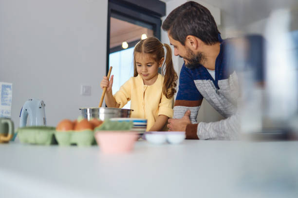 istock Young girl stands at the kitchen table making cakes with her father 1932778832