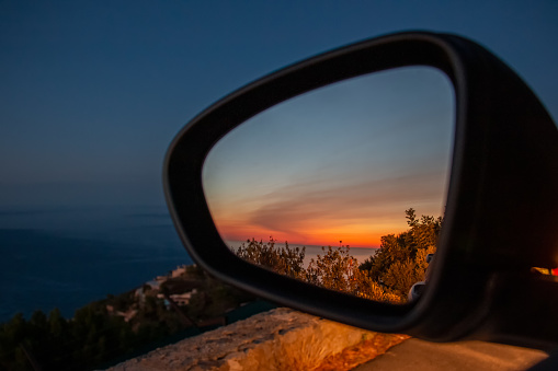 Closeup of a sunset in nature seen from the side mirror of stopped car. Car trip concept