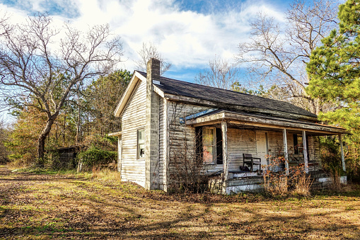 A rustic landscape of an old, abandoned farmhouse with a front porch in North Carolina in the United States.